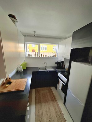 A compact kitchen with a window, a sink, a stove, and a refrigerator. - Cozy 1-bedroom apartment in Reykjavík city center (Reykjavík)