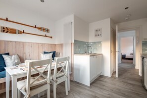 Une cuisine moderne avec des meubles blancs, un îlot central et un coin repas comprenant des chaises et une table, le tout dans des tons blancs.