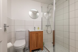 Une salle de bain comprenant des toilettes, un meuble en bois, un lavabo, un miroir et une douche séparée par une paroi en verre.