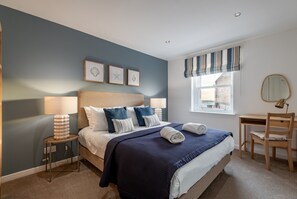 Une chambre à coucher avec un lit, des lampes de chevet, un bureau et une fenêtre avec des rideaux.
