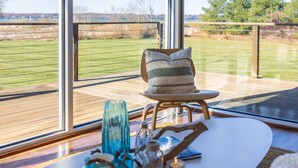 A modern room with large windows, a round table with decorative items, and a cushioned chair. - East Bay 7BR Luxury Home, Beach, Dock, Hot-tub! (Williamsburg)
