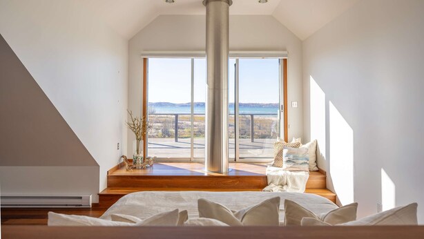 A bedroom with a large bed, a view of the outdoors, and a tall, cylindrical column in the center. - East Bay 7BR Luxury Home, Beach, Dock, Hot-tub! (Williamsburg)