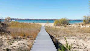 A wooden boardwalk leading to a beach with clear blue water and a distant mountain. - East Bay 7BR Luxury Home, Beach, Dock, Hot-tub! (Williamsburg)