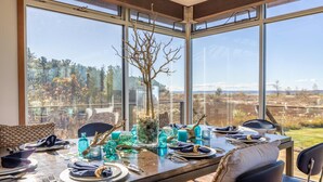 A dining table set for four with a clear view of the outdoors through large windows. - East Bay 7BR Luxury Home, Beach, Dock, Hot-tub! (Williamsburg)