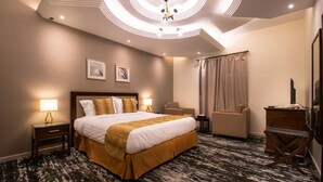 A hotel room with a large bed, a desk, a chair, a dresser, and a ceiling light fixture. - Golden Rose Hotel (Jizan)