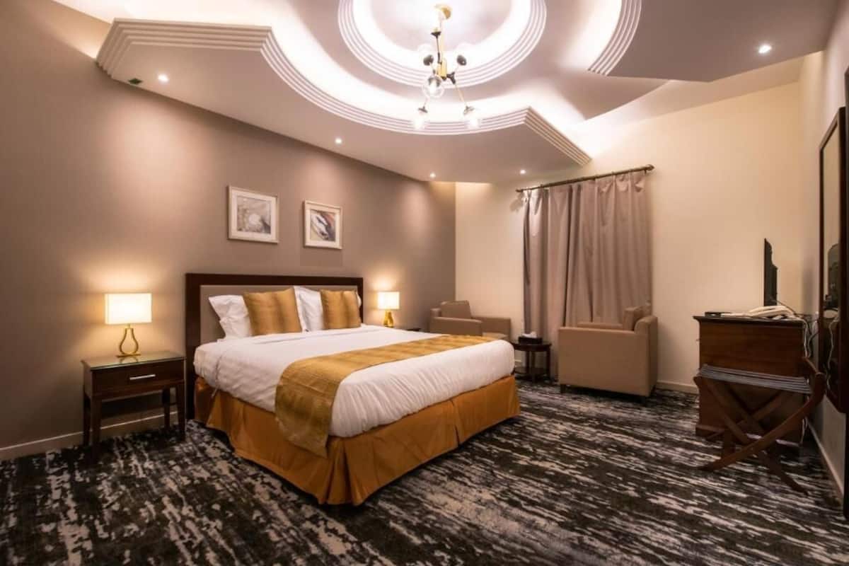A hotel room with a large bed, a desk, a chair, a dresser, and a ceiling light fixture.