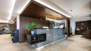 A reception area with a modern design, featuring a reception desk, potted plants, and a wooden slatted ceiling. - Golden Rose Hotel (Jizan)