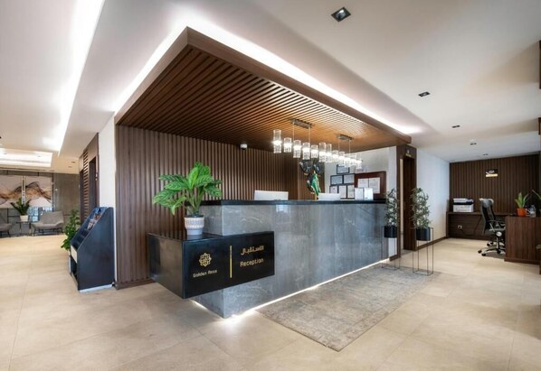 A reception area with a modern design, featuring a reception desk, potted plants, and a wooden slatted ceiling. - Golden Rose Hotel (Jizan)