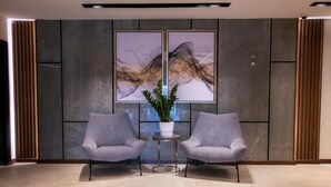 A modern lobby with two grey armchairs, a small round table, and a potted plant. - Golden Rose Hotel (Jizan)