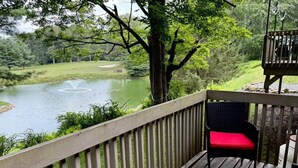 Une terrasse en bois avec une chaise et une table, donnant sur un étang et une végétation luxuriante.