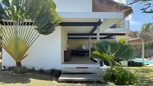 Een modern huis met twee verdiepingen en een plat dak, met een zichtbare keuken en een zwembad op de achtergrond.