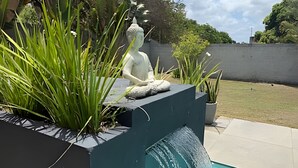 Een tuin met een waterpartij, inclusief een beeld en beplanting.