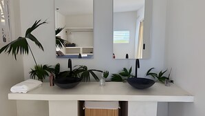 Een badkamer met een witte wastafel, twee zwarte wasbakken en verschillende potplanten.