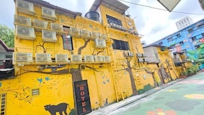A yellow building with multiple air conditioning units, a 'HOTEL' sign, and a mural of a tree and a cat. - Red Velvet Inn Bukit Bintang (Kuala Lumpur)