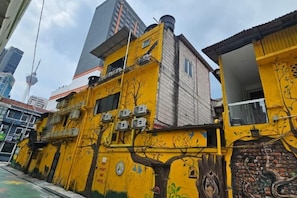 A yellow building with a tree mural, air conditioning units, and a view of a tall tower in the background. - Red Velvet Inn Bukit Bintang (Kuala Lumpur)