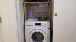 Lavanderia compacta com máquina de lavar Bosch e micro-ondas numa prateleira.