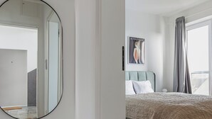Une chambre à coucher moderne avec un grand miroir, un lit avec une tête de lit, un banc et une fenêtre avec des rideaux.
