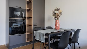 Un coin repas comprenant une table, des chaises, un vase avec des fleurs séchées et un four encastré.