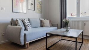 Un salon moderne avec un canapé gris, une table basse et des œuvres d’art encadrées accrochées au mur.