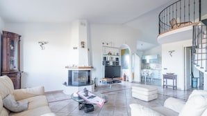 Een ruime woonkamer met een open haard, een eethoek en een keuken op de achtergrond.