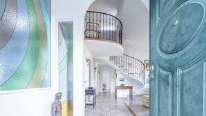 Een ruime binnenruimte met een gebogen trap, een grote blauwe deur en een decoratieve glazen wand.