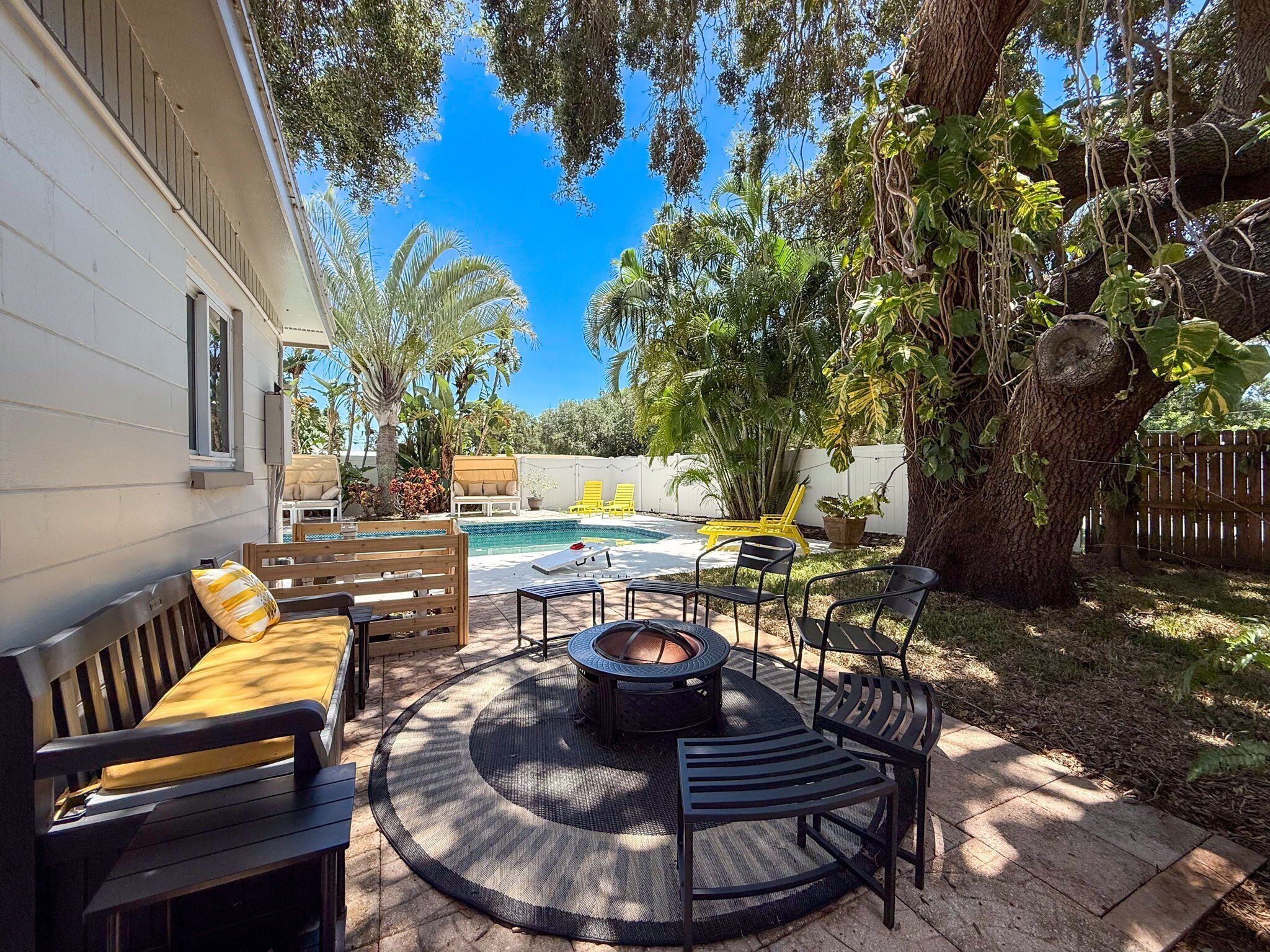 A backyard with a pool, outdoor furniture, and a large tree.