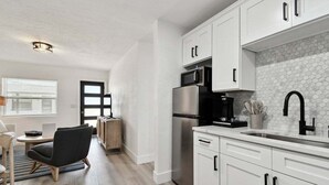 Een moderne keuken met witte kasten, een roestvrijstalen koelkast, een magnetron en een koffiezetapparaat.