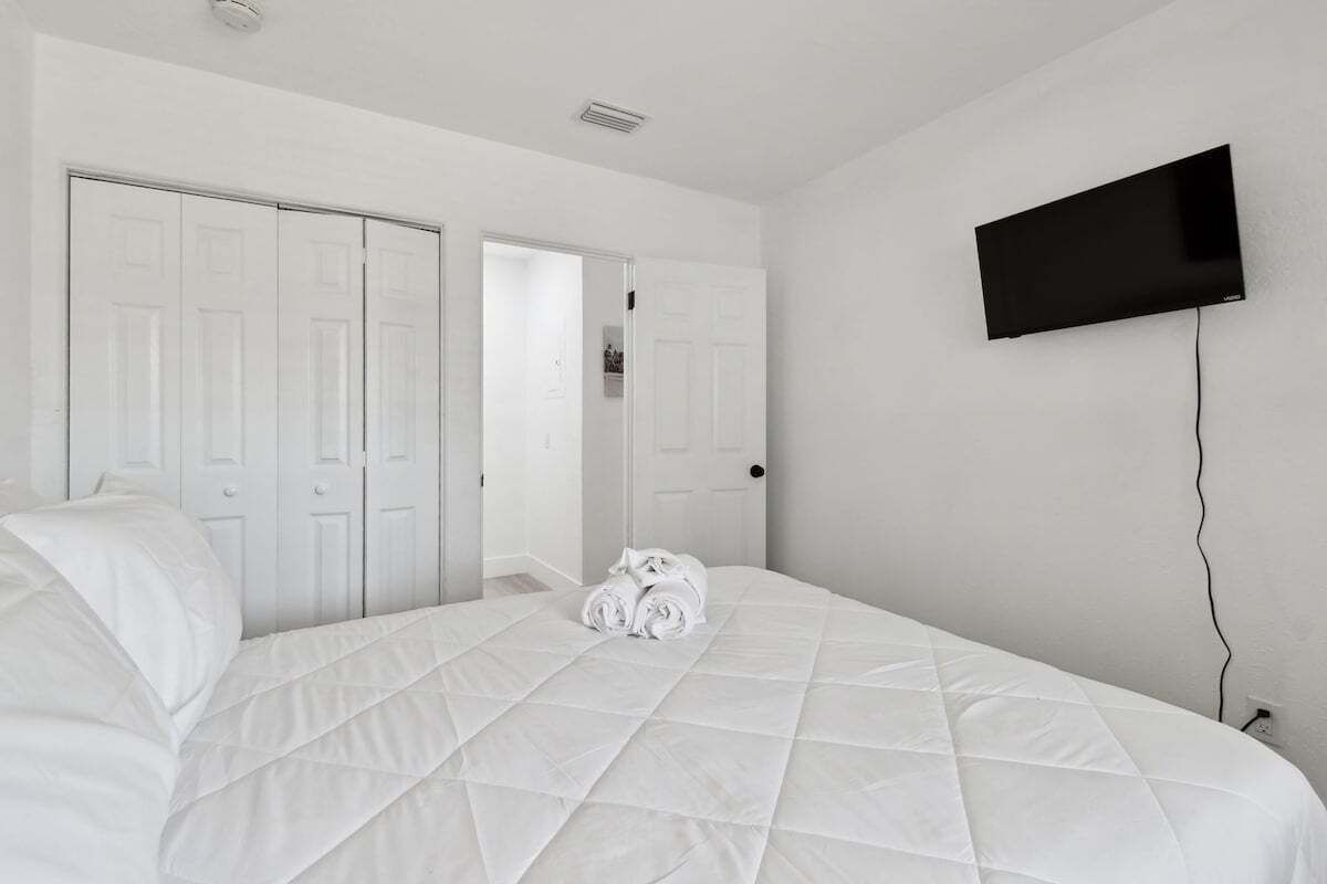 Habitación de hotel con una cama grande, un televisor de pantalla plana en la pared y un juego de puertas blancas.