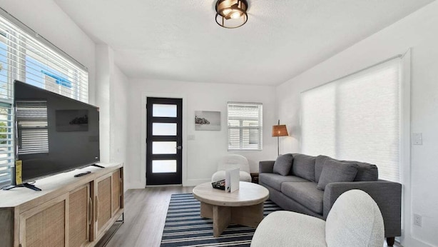 Una sala de estar moderna con televisor de pantalla plana, sofá gris, sillón blanco y una mesa redonda.