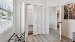 Un pasillo con puertas blancas, un banco y un cuadro en la pared.