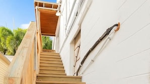 Eine Holztreppe mit schwarzen Metallankern, die zu einem weißen Gebäude mit einem Fenster und einer Holzdielenveranda führt.