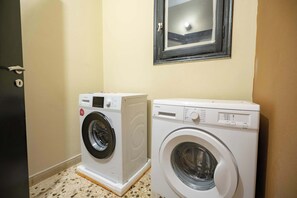 Two front-loading washing machines in a laundry room with a door and a window above. - Warm 2BR Apt • Central Kypseli by ΜΡS (Athina)