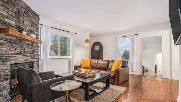 A living room with a stone wall, a fireplace, a brown leather sofa with yellow cushions, a dark coffee table, and a round side table. - Omaha Escape Central Getaway with Private Sauna! (Omaha)