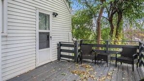 A covered porch with a black railing, two wicker chairs, and a small table. - Omaha Escape Central Getaway with Private Sauna! (Omaha)