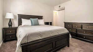 Un dormitorio con cama, mesitas de noche, cómoda y una puerta.