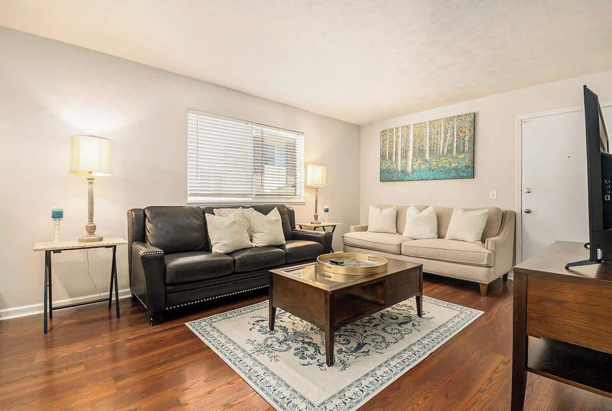 A living room with a black leather sofa, a beige sofa, a coffee table, and a painting on the wall.