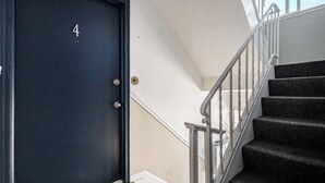 Una puerta negra con el número 4, una escalera con alfombra y barandillas metálicas, y una pared blanca.