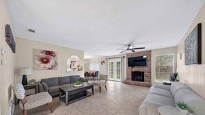 A spacious living room with a fireplace, a ceiling fan, and a dining area with a table and chairs. - Modern 5BR Home |Cozy Fireplace, Office & Downtown (Austin)