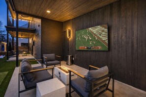 Eine Terrasse im Freien mit Sitzgelegenheiten, einem Feuerkorb und einem großen Bildschirm, auf dem ein Fußballspiel läuft.
