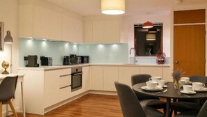 A modern kitchen with white cabinets, a built-in oven, and a dining area with a table set for four. - 2-Bedroom flat - Central London - Trafalgar Square (London)
