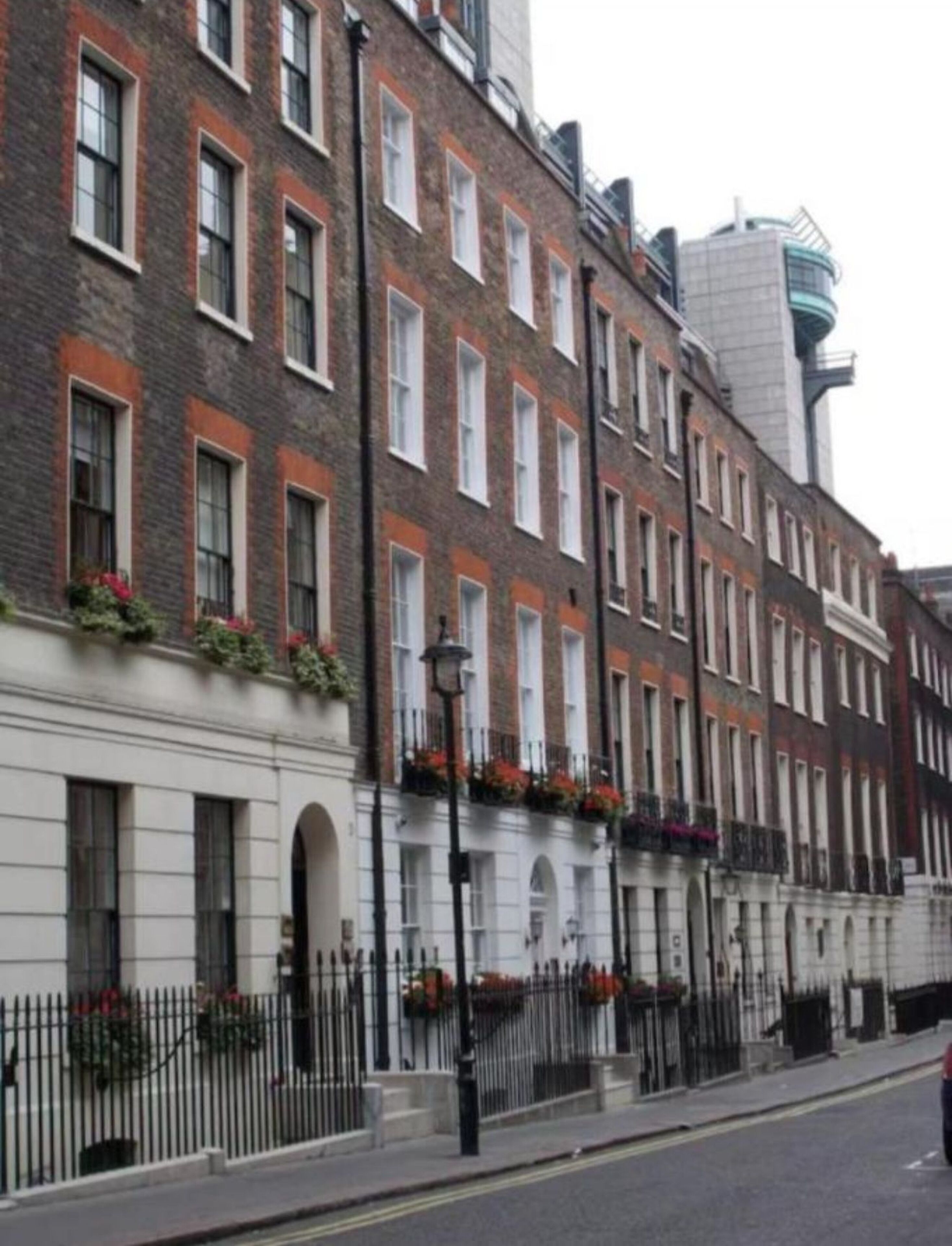 A row of brick townhouses with white window frames, a black metal fence, and a street lamp.