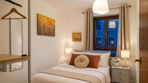 A hotel room with a bed, bedside tables, a hanging light fixture, a window with curtains, and artwork on the wall. - 2-Bedroom flat - Central London - Trafalgar Square (London)