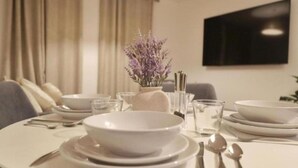 A dining table set with white plates, bowls, and cutlery, a vase with purple flowers, and a flat-screen TV mounted on the wall. - 2-Bedroom flat - Central London - Trafalgar Square (London)