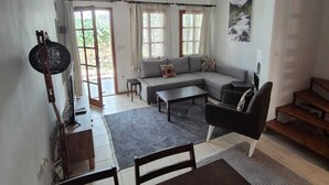 A spacious living room with a sofa, coffee table, and dining table. There is a ceiling fan, a window with curtains, and a painting on the wall. - Serene building with AC in beautiful Bodrum (Bodrum)