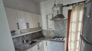 A compact kitchen with white cabinets, a gas stove, a dishwasher, and a refrigerator. - Serene building with AC in beautiful Bodrum (Bodrum)