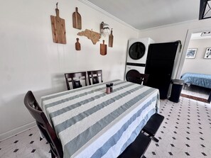 Un coin repas avec une nappe à rayures, des chaises en bois, un banc et un lave-linge fixé au mur.