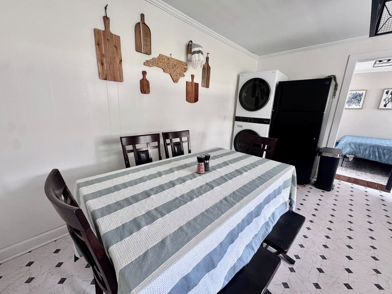 Un comedor con una mesa dispuesta para cuatro, sillas, una lavadora y una cama al fondo.