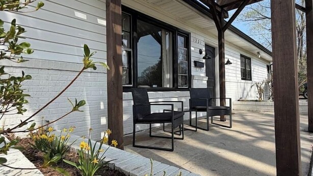 A covered patio with a wooden pergola, a white building with a number '1231' on the door, and a seating area with two chairs. - Hidden Getaway | Fire Pit | 1K,2Q/1 bath (Eden)