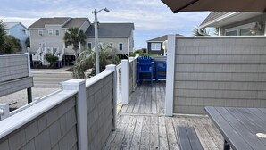Eine Holzterrasse mit einem Picknicktisch und blauen Stühlen, einem weißen Zaun und Häusern im Hintergrund.