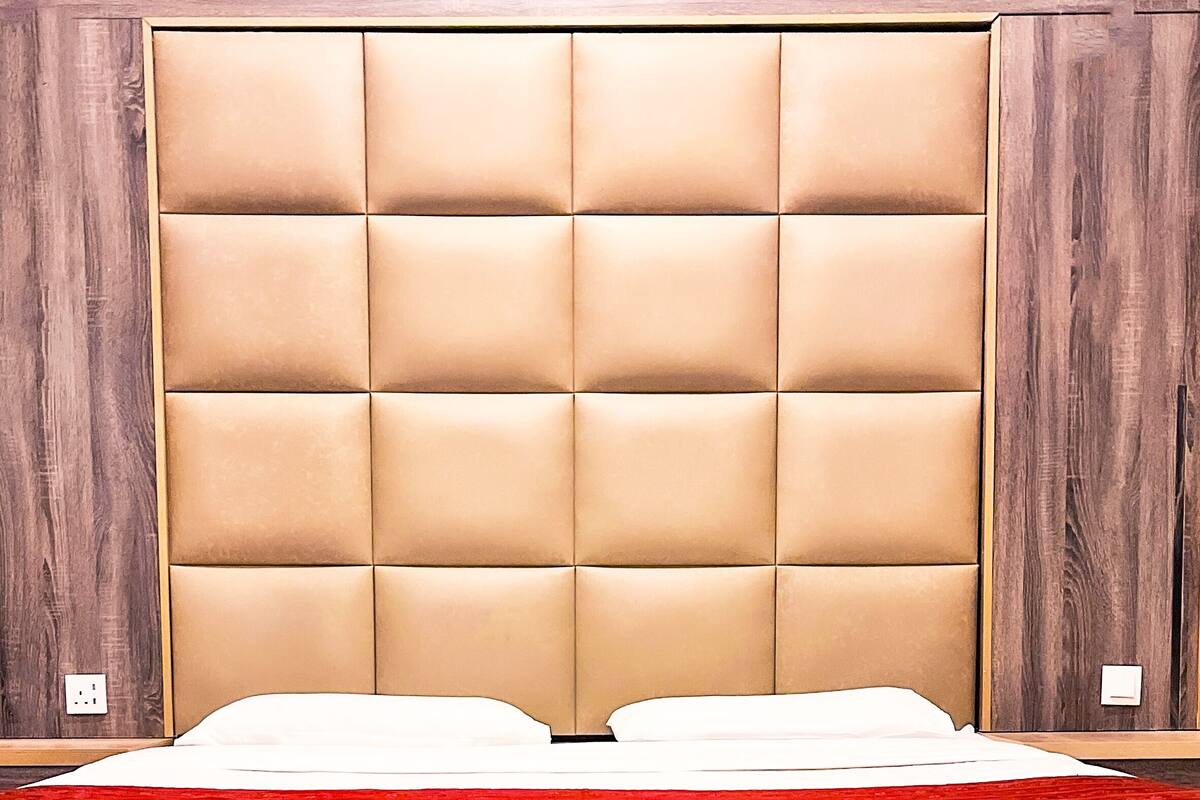 A bed with a padded headboard, wooden paneling on the sides, and a red accent at the foot of the bed.